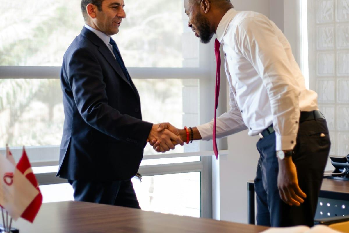 Two colleagues shaking hands across a desk after a meeting