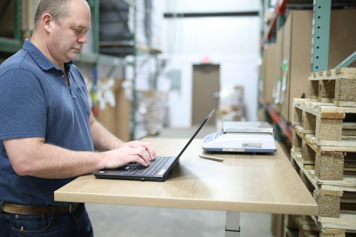 A warehouse supervisor working at a laptop beside the racking